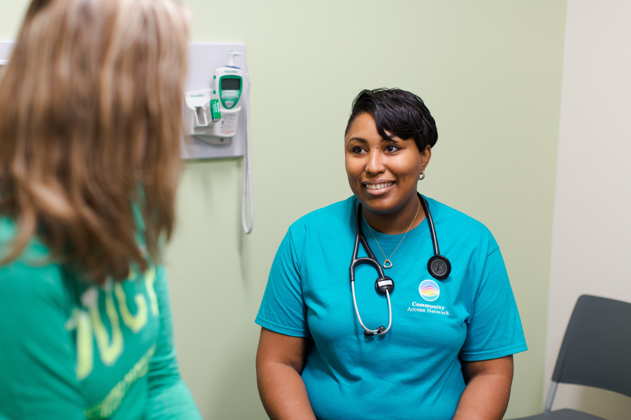 female nurse wearing a blue community access network shirt speaks to a female patient wearing a green shirt