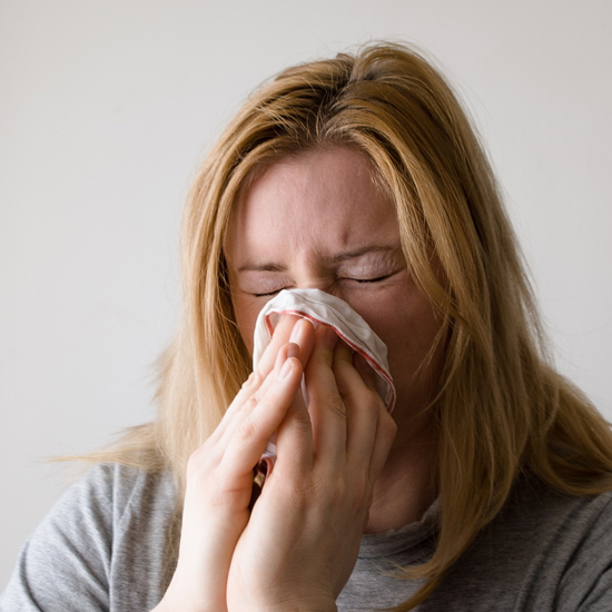a woman blows her nose because of her allergy symptoms