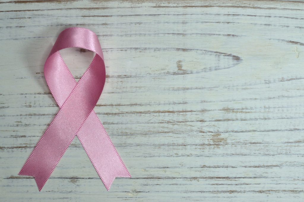 a pink breast cancer ribbon sits on a wooden table