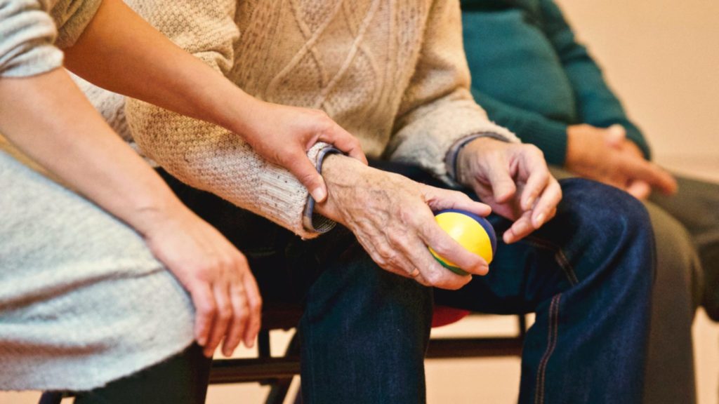 a female caregiver holds the hand of an older man while he practices with a stress ball