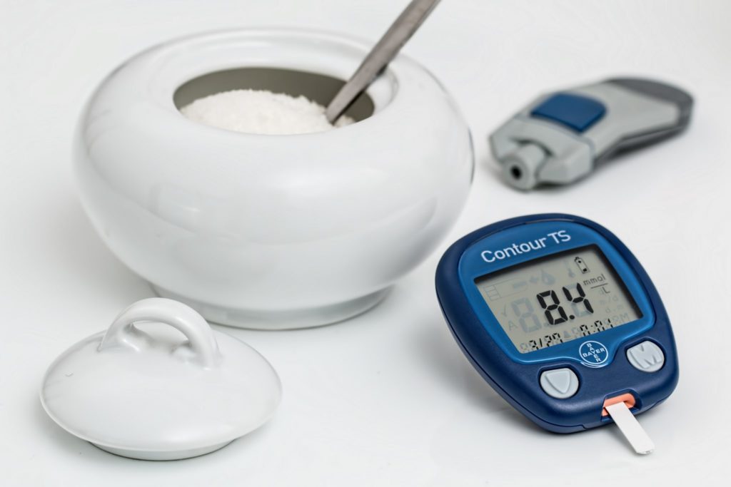 a blue blood sugar testing device sits next to a bowl of sugar