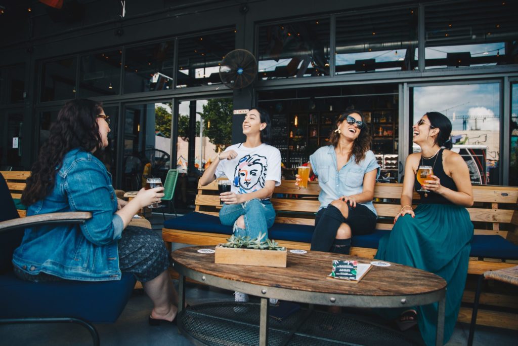 four women smile and laugh over coffee