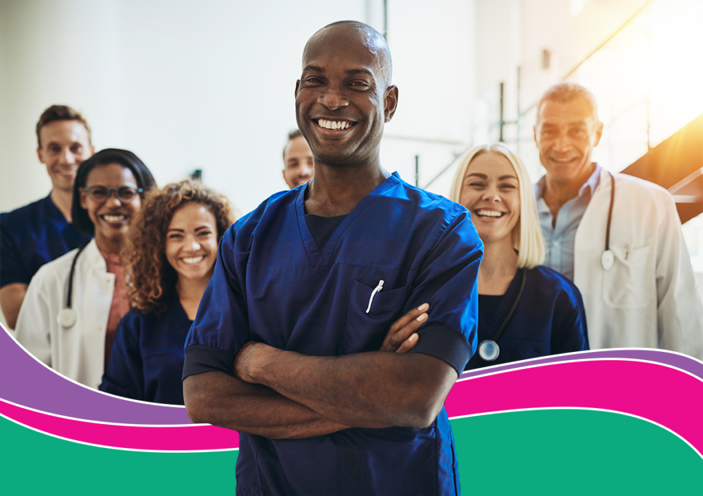 A Black male doctor smiles in front of four of his coworkers.