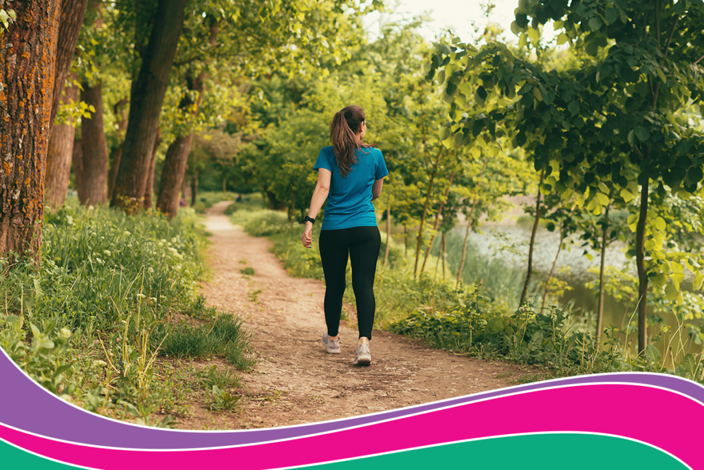 A women walks outdoors through a forest next to a river.